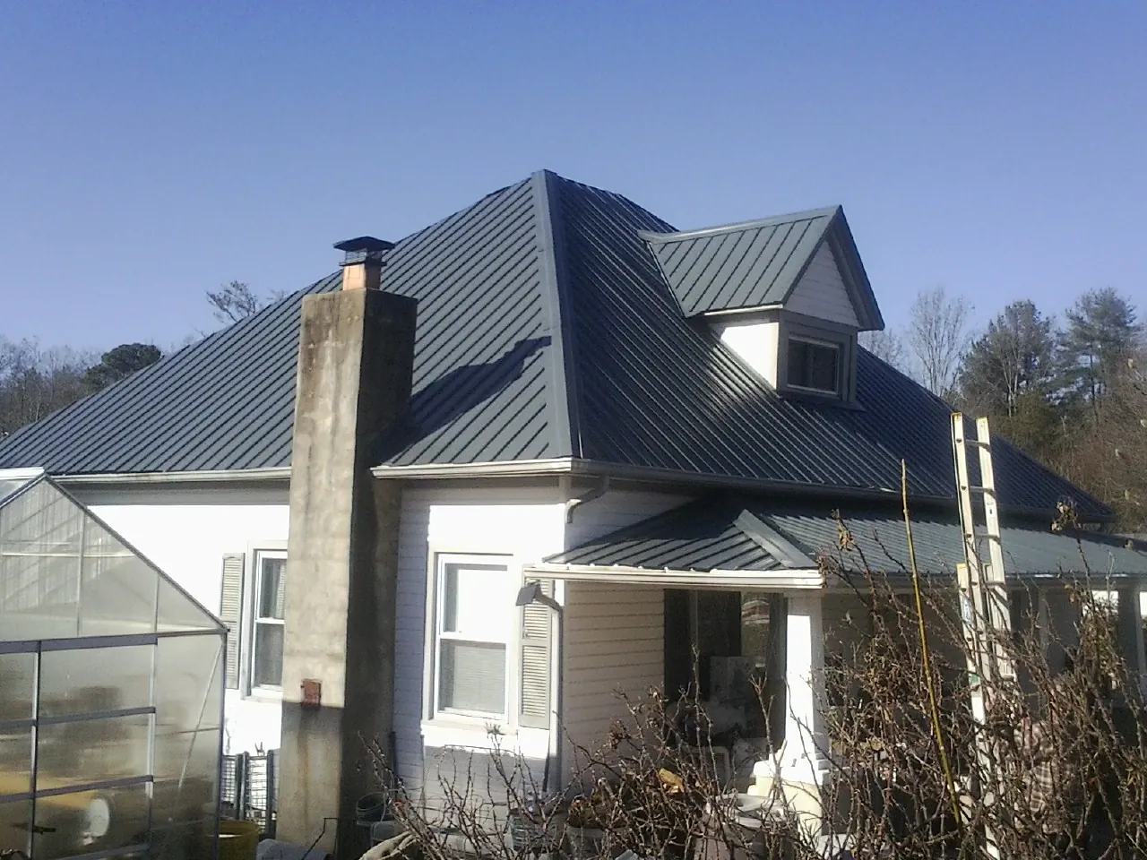 Dark blue standing seam metal roof on a white farmhouse with dormer — Slate & Tile Roof Repair by Roofing Brothers in Cogswell