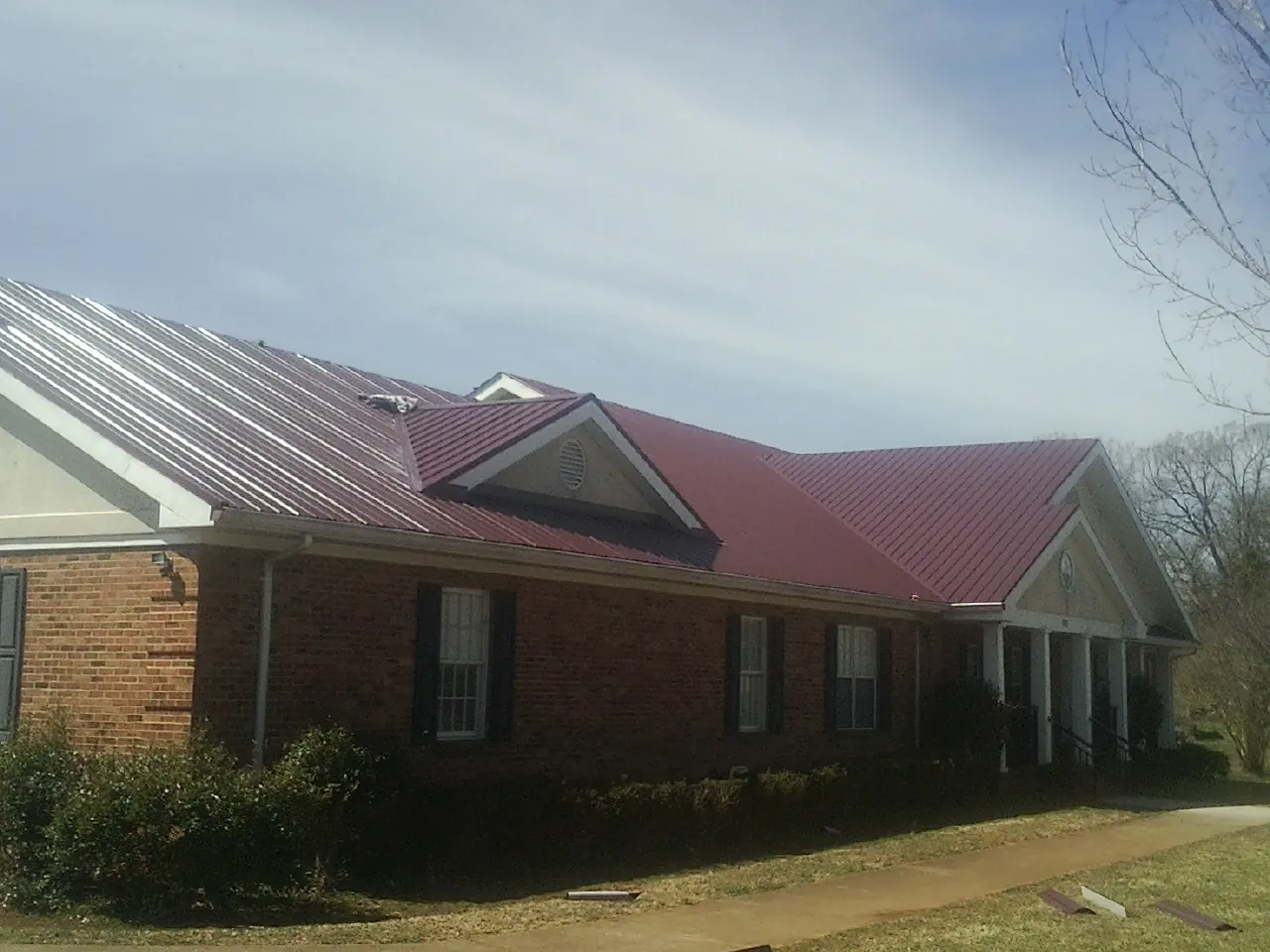 Red metal roof with gabled entries on a long brick building, from a Hail Damage Roof Repair job in Cogswell