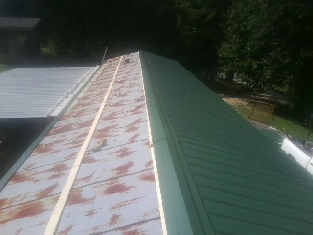 Old rusted panels beside newly installed green metal roofing — Wind Damage Roof Repair by Roofing Brothers in Cogswell