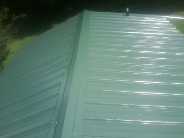 New green metal panels meeting at the ridge of a roof — Flat Roof Repair work by our crew in Cogswell