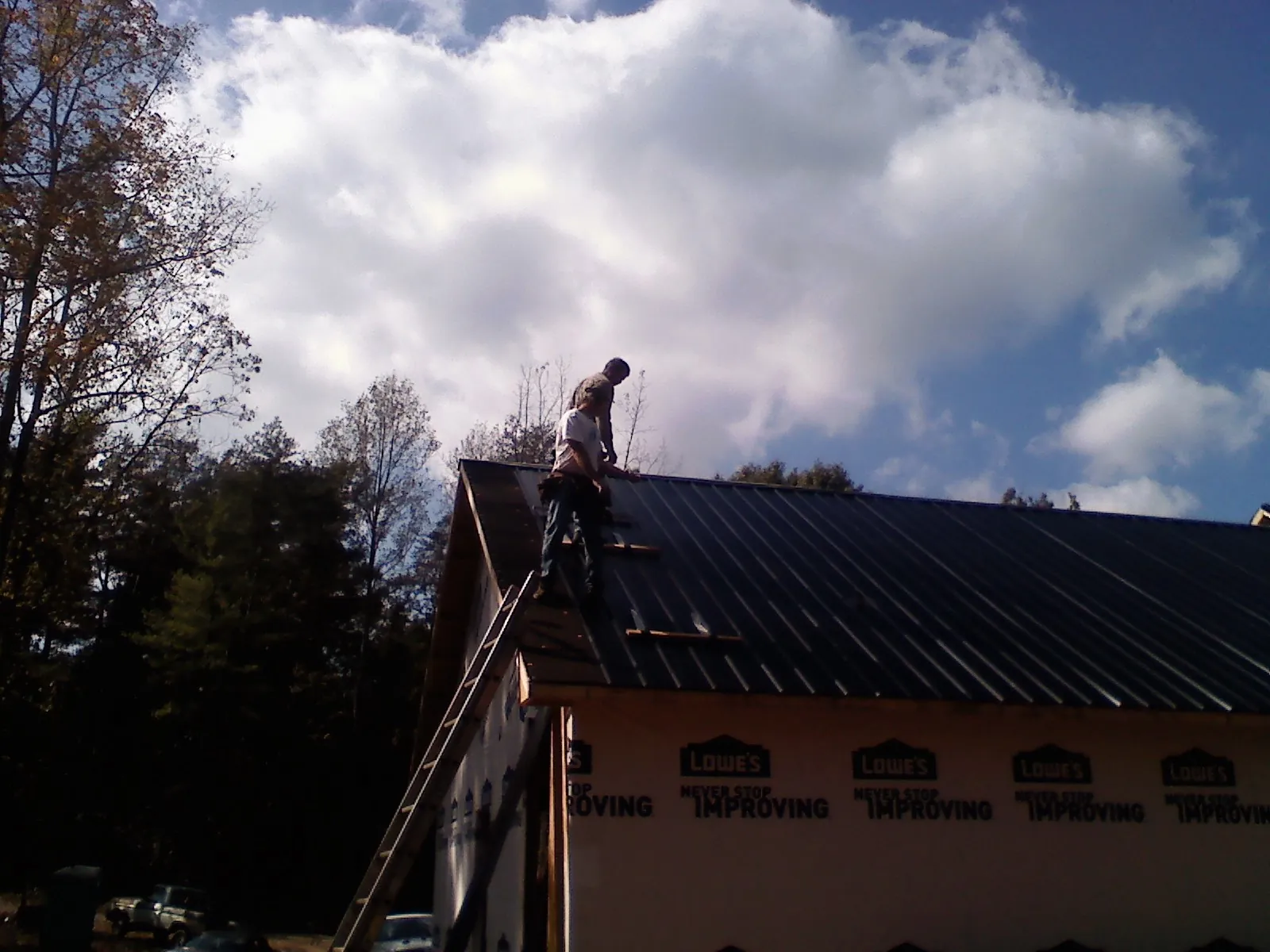 Roofer fastening dark metal panels high against a cloudy sky, from a Roof Inspection job in Cogswell