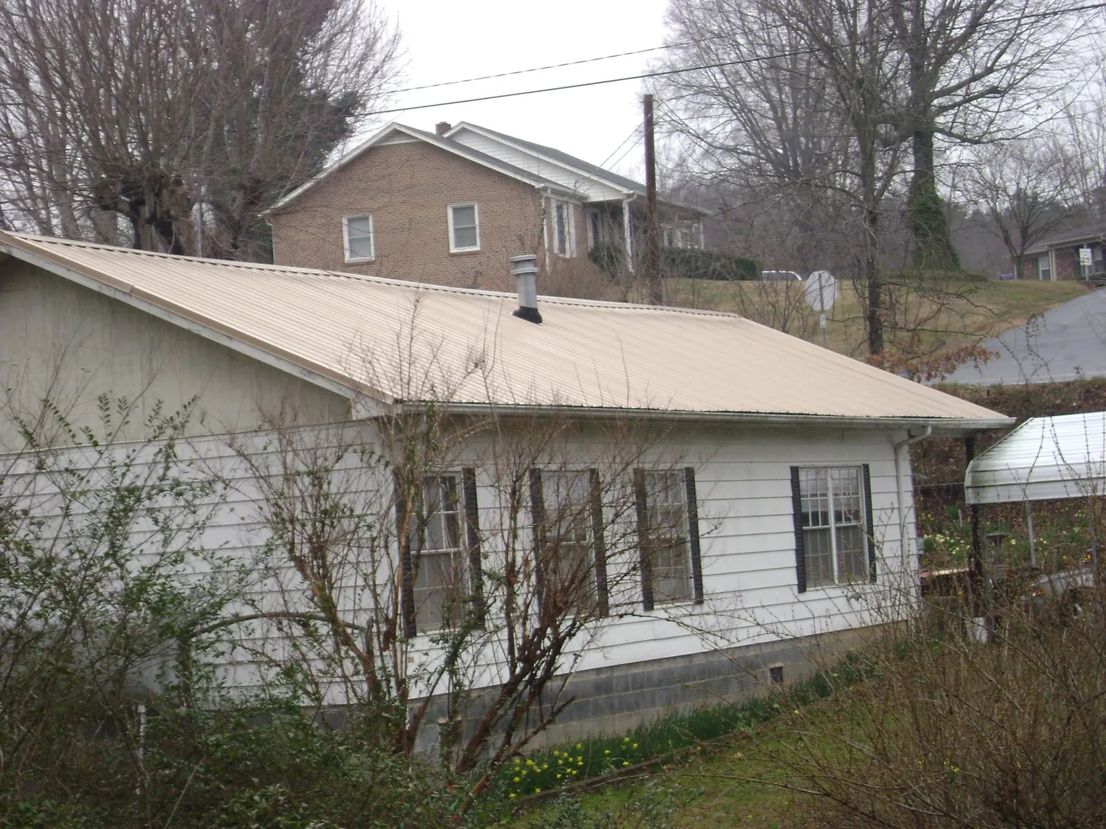 Tan metal roof on a white sided house set into a hillside — Commercial Roofing by Roofing Brothers in Cogswell