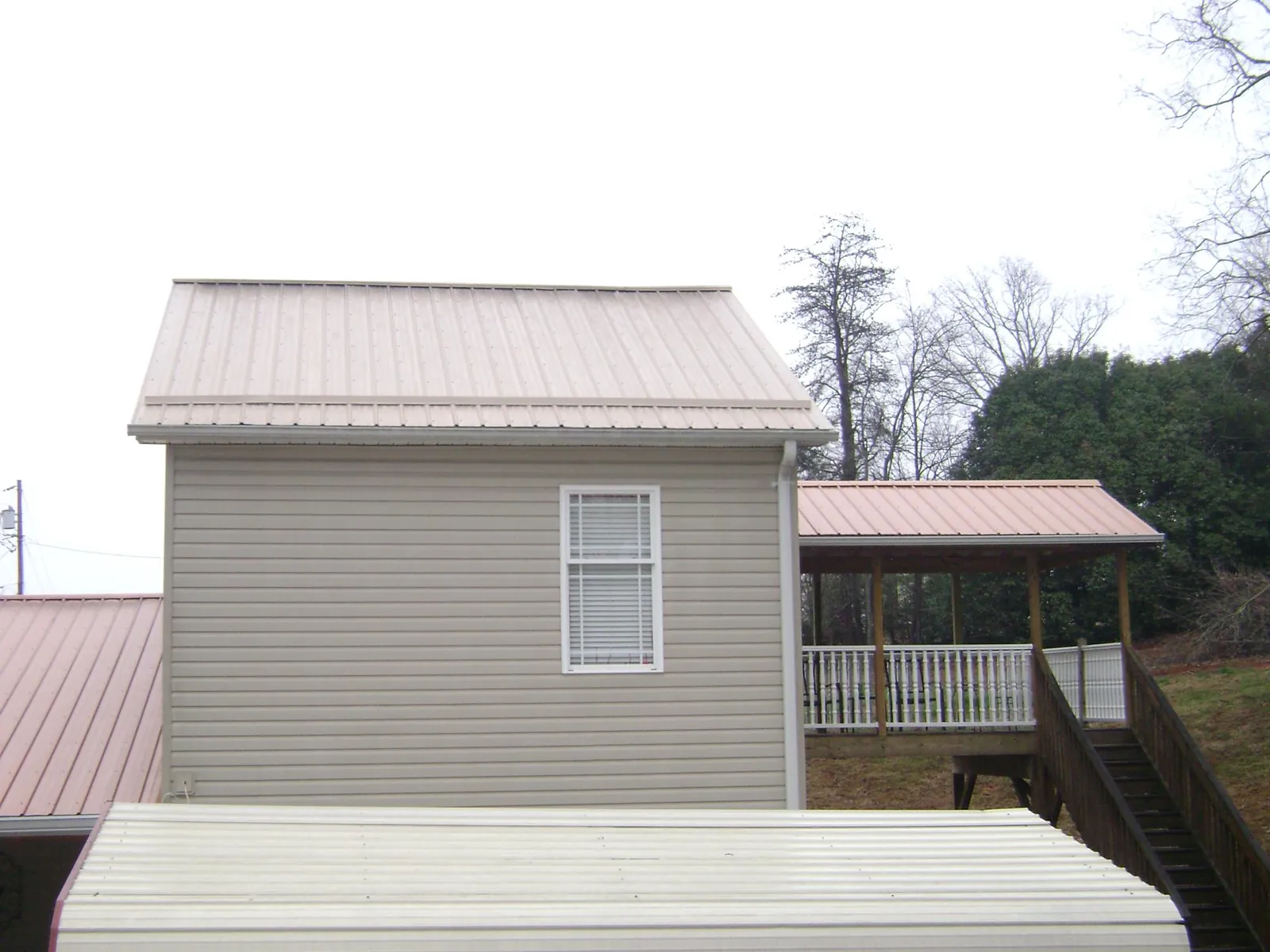 Tan metal roofs on a two story addition and attached porch, from a Roof Replacement job in Cogswell